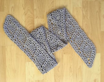 May include: A long, crocheted scarf in a light gray color. The scarf is made with a delicate, openwork pattern.