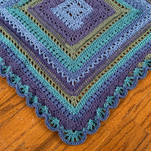 May include: A crocheted blanket with a scalloped edge in shades of blue, green, and purple.