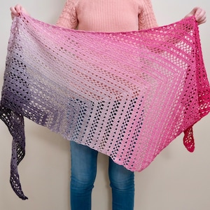 Peut inclure: Un châle fait à la main, à tissage ouvert, dans un dégradé de couleurs, passant du violet foncé au rose clair et au fuchsia vif. Le châle est tenu, mettant en valeur son motif de crochet complexe et sa texture délicate. Un bel accessoire.