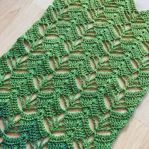 May include: A green crochet shawl with a leafy pattern. The shawl is made with a gradient yarn that transitions from a darker green to a lighter green.
