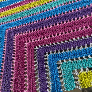 Peut inclure: Une couverture en crochet colorée avec un motif carré dans des tons de rose, violet, bleu, vert et jaune.