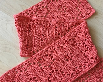 May include: A coral-colored crocheted scarf with a lacy pattern. The scarf is folded in half and the ends are overlapping.
