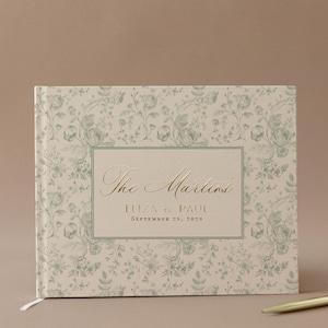 May include: A hardcover guest book with a floral pattern in light green and cream. The book features gold lettering that reads "The Martins," along with the names Eliza & Paul and the date September 29, 2025.