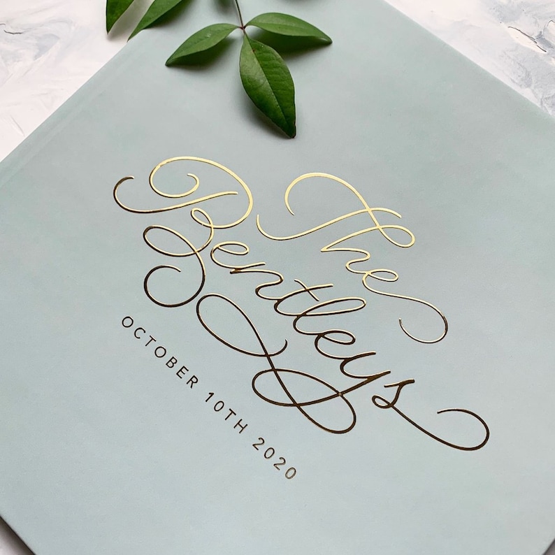 May include: A light blue book cover with gold script text that reads "The Bentleys" and the date "October 10th 2020". A sprig of green leaves is in the upper corner.