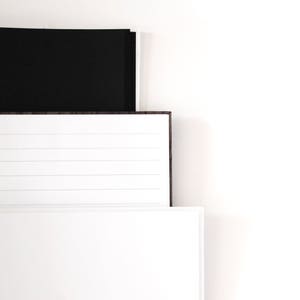 May include: A stack of three notebooks with white and black covers. The middle notebook has lined pages, while the bottom one has blank pages. The notebooks are arranged against a white background.