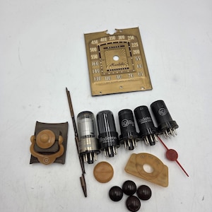 May include: A collection of vintage radio parts, including vacuum tubes, a dial face with the "Mantola" brand, and various other components. The parts are in shades of brown, black, and tan, with some metal elements.