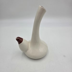 May include: A cream-colored ceramic pitcher with a long, curved spout and a bulbous base. The spout and the inside of the pitcher's opening are dark brown. The pitcher has a unique, organic shape and a crackled glaze.