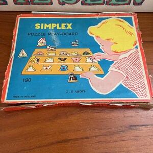 May include: A vintage Simplex puzzle play-board box with a blue background and colorful illustrations. The box features a child playing with the puzzle, and the text "SIMPLEX PUZZLE PLAY-BOARD" is visible. The box is designed for children aged 2-5 years.