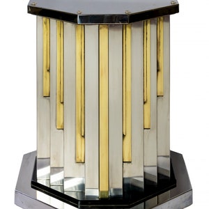 May include: Octagonal pedestal table with a silver and gold geometric design. The table has a polished metal finish and a black base.