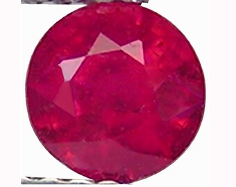 May include: A round, faceted ruby gemstone with a deep red color. The gemstone is set in a silver setting.