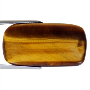 Puede incluir: Una piedra preciosa de ojo de tigre lisa, rectangular y pulida, de color marrón dorado con un efecto chatoyante.