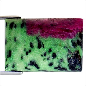 May include: A green and pink gemstone with black inclusions. The gemstone is rectangular and has a smooth, polished surface.