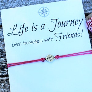 May include: A red friendship bracelet with a compass charm and a card that reads "Life is a Journey best traveled with Friends! ...and as you do, wear this bracelet as a reminder of the joy you bring to my life. true!"