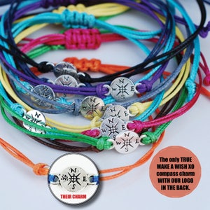 May include: A collection of colorful friendship bracelets with silver compass charms. Each bracelet is tied with a knot and features a different color of string. The charms have a compass design with the letters N, S, E, and W.