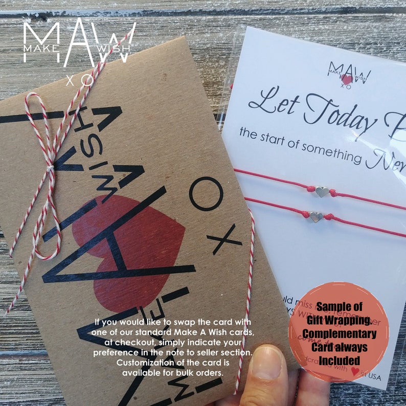 May include: A kraft paper card with the text "Make A Wish" and a red heart. The card is tied with red and white twine. A separate card with the text "Let Today Be the start of something New" and two red string bracelets with silver heart charms. The text "Sample of Gift Wrapping. Complementary Card always Included" is visible.