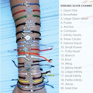 May include: A close-up of a person's arm wearing 20 different bracelets with sterling silver charms. Each bracelet is a different color and has a different charm. The charms include a star, snowflake, heart, puzzle piece, anchor, compass, infinity hearts, three circles, hamsa hand, small flower, puffy heart, branch, knot, wing, skinny heart, large infinity, small infinity, petite infinity, arrow, and solid star.