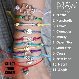 May include: A close-up of a person's wrist wearing eleven colorful bracelets with different charms, including a puzzle, handcuffs, arrow, compass, infinity symbol, open star, solid star, cross, paw print, heart, and apple. The bracelets are made of string and the charms are silver. The text "SELECT YOUR CHARM" is visible in the lower left corner of the image. The text "MAKE A WISH XO" is visible in the upper right corner of the image. The text "1. Puzzle" through "11. Apple" is visible on the right side of the image.