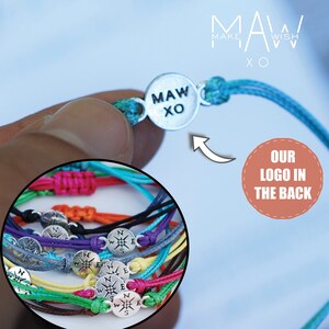 May include: A close-up of a colorful set of bracelets with compass charms. The bracelets are made of thin, braided cords in various colors, including red, orange, yellow, green, blue, and purple. Each bracelet has a silver compass charm with the letters N, S, E, and W inscribed on it. The bracelets are arranged in a circle, with the compass charms facing outward. The image also shows a single bracelet with a silver charm that says "MAW XO".