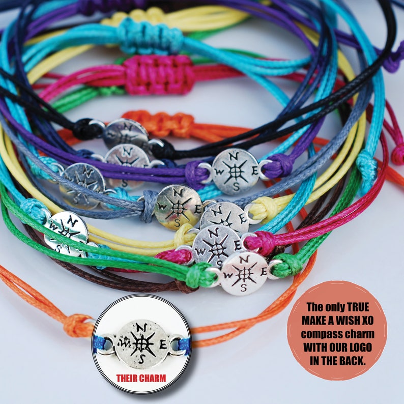 May include: A collection of colorful friendship bracelets with silver compass charms. Each bracelet is tied with a knot and features a different color of string. The charms have a compass design with the letters N, S, E, and W.