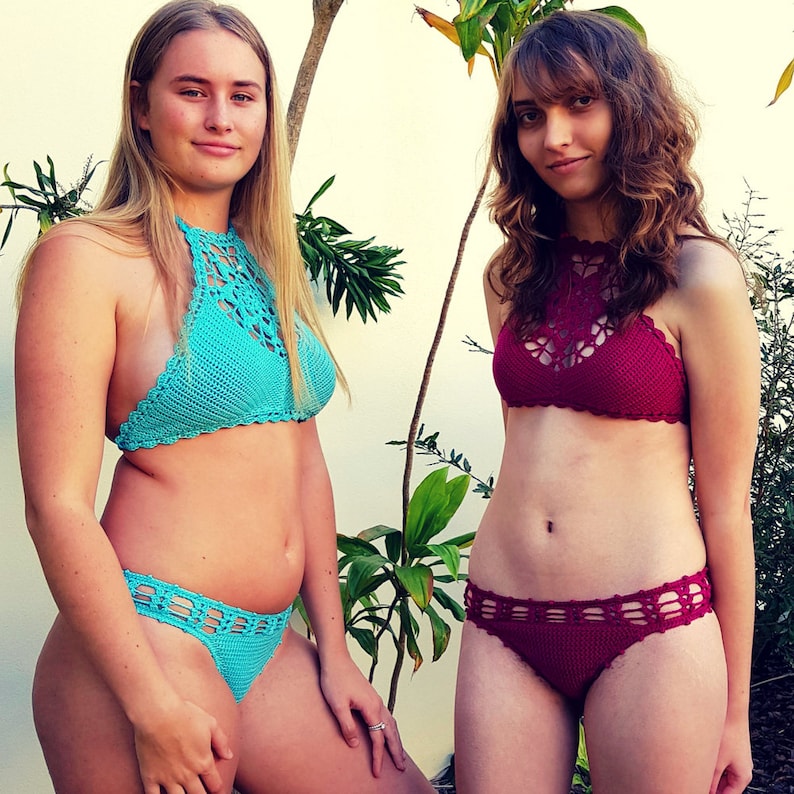 May include: Two crochet bikinis. One is turquoise, the other is burgundy. Both have halter tops and matching bottoms. The turquoise bikini is worn by a person with long blonde hair. The burgundy bikini is worn by a person with brown hair.