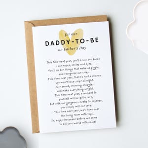 A white folded greeting card laying flat on top of a kraft brown envelope. The design reads "for our daddy-to-be on Father's day" in black modern fonts. A yellow heart design sits behind the title. Our original poem from the baby bump to their soon-to-be parent is below in fun, playful black fonts (for wording, go to our description)