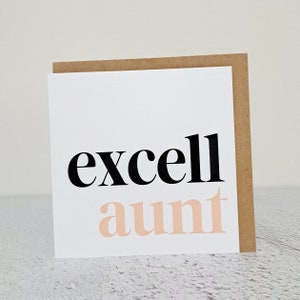 May include: A white card with black text that says "excell" and pink text that says "aunt". The card has a brown envelope.