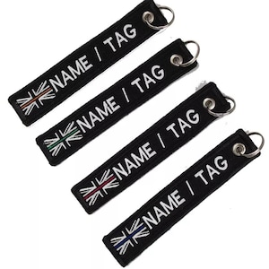 May include: Four black fabric keyrings with the text "NAME / TAG" in white. Each keyring features a different coloured Union Jack flag design. The keyrings have a metal ring for attachment.