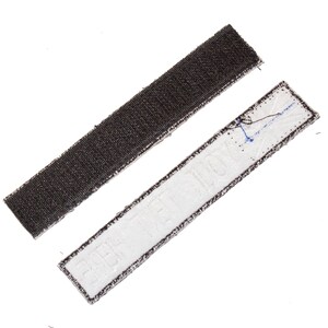 May include: A close-up of two pieces of hook and loop fastener tape. One piece is black and the other is white with the text "HIT THE DECK" printed on it.