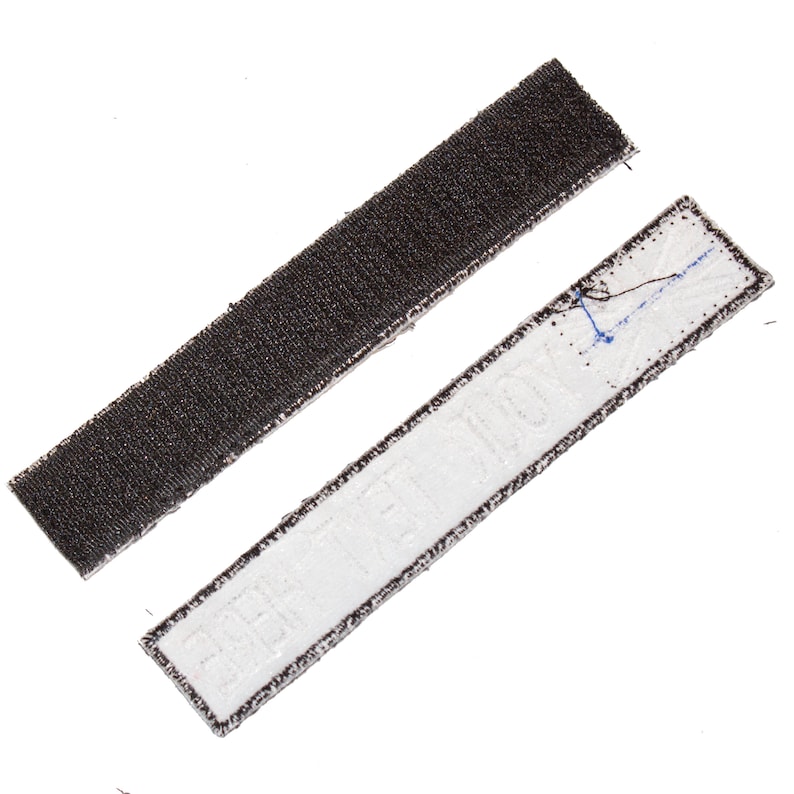 May include: A close-up of two pieces of hook and loop fastener tape. One piece is black and the other is white with the text "HIT THE DECK" printed on it.