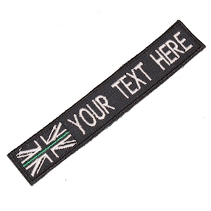 May include: Black embroidered patch with a white Union Jack flag with a green stripe across the middle and the text "YOUR TEXT HERE" in white.