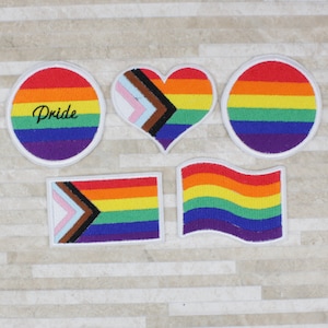 May include: Five embroidered patches with rainbow designs. One patch is a circle with the word "Pride" in the centre. Another patch is a heart shape. The other three patches are rectangular with different rainbow designs.