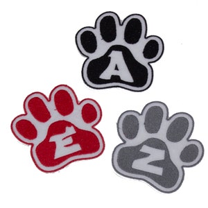 May include: Three embroidered paw print patches in black, red, and grey. Each paw print has a white letter: A, E, and Z. The patches are likely for clothing or accessories.