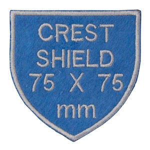 May include: A blue felt shield patch with white embroidered text that reads "CREST SHIELD 75 X 75 mm".