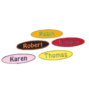 May include: Five oval-shaped embroidered name tags with different names and colours. The names are "Robin", "Robert", "Jessica", "Thomas", and "Karen".