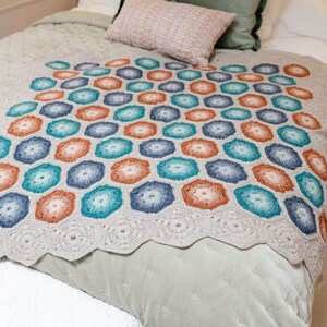 Peut inclure: Une couverture en crochet avec un motif géométrique dans les tons de bleu, turquoise et orange. La couverture est réalisée avec un point nid d'abeille et a un fond blanc.