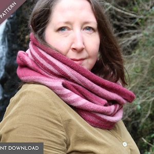 May include: A woman wearing a pink and burgundy striped infinity scarf. The scarf is knit and has a soft, textured look. The woman is standing in front of a waterfall.
