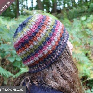 May include: A knitted beanie featuring a multi-colored horizontal striped pattern in shades of navy blue, magenta, olive green, and grey. The hat has a ribbed brim and a textured stitch design. The image includes text reading PDF KNITTING PATTERN.