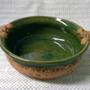 May include: A green ceramic bowl with two decorative handles. The bowl has a brown rim and a brown base with a geometric pattern.