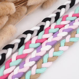 Könnte beinhalten: Nahaufnahme von vier geflochtenen Kordeln in verschiedenen Farben. Die Kordeln sind schwarz, grau und weiß; rosa, mintgrün und weiß; lila, rosa, mintgrün und beige; und beige, mintgrün und rosa. Die Kordeln sind diagonal angeordnet.