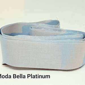 May include: A roll of Moda Bella Platinum fabric in a light blue and white colorway. The fabric is folded and rolled up, showing the pattern and texture.