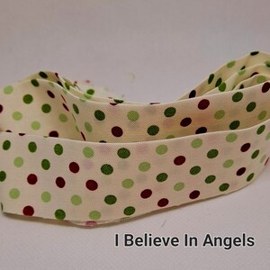 May include: Cream-colored fabric ribbon with green and burgundy polka dots. The ribbon is folded in half and the text "I Believe In Angels" is printed below the ribbon.