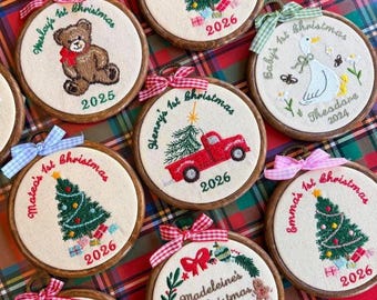 Può includere: Una collezione di telai da ricamo circolari in legno con centri in tessuto che presentano disegni ricamati a mano, tra cui un orsacchiotto, un camion rosso, un'oca e alberi di Natale, personalizzati con nomi e gli anni 2024, 2025 o 2026.