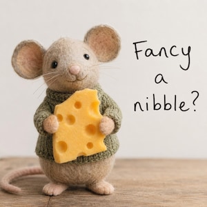 Op de afbeelding: Een handgemaakte vilten muis met een groene trui, die een groot stuk gele kaas vasthoudt. De muis heeft een lange staart en snorharen. Tekst rechts: "Fancy a nibble?"