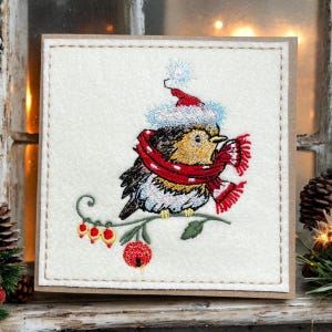 a* Une carte de Noël brodée à la main. Robin brodé très détaillé avec son chapeau de fête et son écharpe, prêt pour les fêtes
