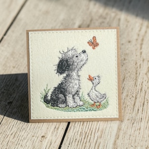 Peut inclure: Une carte de vœux carrée présentant une illustration brodée d'un chien gris au pelage duveteux assis à côté d'un petit caneton blanc. Un papillon orange est brodé au-dessus du chien sur un carré de tissu de couleur crème.