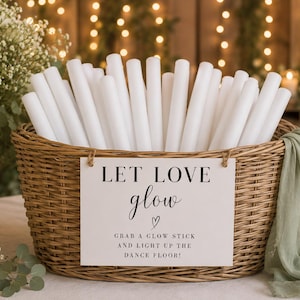 Può includere: Un cesto in vimini intrecciato marrone riempito con numerosi bastoncini luminosi cilindrici bianchi. Un cartello rettangolare bianco è appeso sul davanti con il testo nero: LET LOVE glow, GRAB A GLOW STICK AND LIGHT UP THE DANCE FLOOR! e un cuoricino.