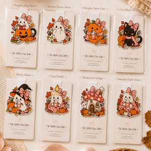 May include: Eight individual bookmarks featuring autumn-themed illustrations of ghosts, a black cat, a candle, a mushroom cottage, and pumpkins, each adorned with a pink plaid bow. The bookmarks are displayed on branded cards labelled The Happy Cow Shop.