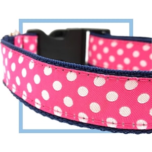 May include: Pink dog collar with white polka dots and a navy blue trim. The collar has a black plastic buckle.