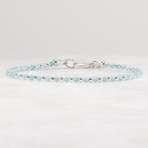 May include: A delicate bracelet featuring a repeating pattern of small, faceted light blue beads and polished silver-toned metallic spheres. The piece is finished with a silver-toned metal lobster claw clasp and a circular jump ring connector.