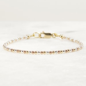May include: Delicate beaded bracelet featuring a mix of silver, gold, and rose gold beads. The bracelet has a small gold clasp. The beads are evenly spaced, creating a simple yet elegant design. A beautiful piece of jewelry.